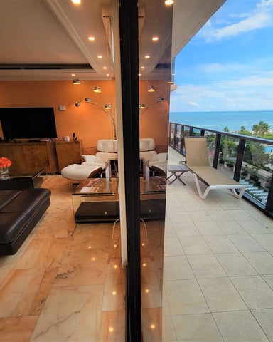 Modern living room with orange walls and marble floors opening to oceanfront balcony with sea and palm tree views