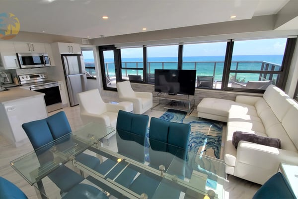 Open-plan beachfront condo with kitchen, dining area, living room, and ocean view through floor-to-ceiling windows