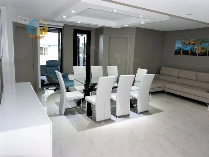 Salon et salle à manger modernes ouverts, avec chaises blanches, table à manger en verre, canapé beige et éclairage encastré au plafond