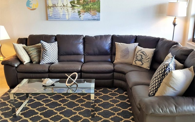 Living room with large dark brown leather sectional sofa, glass coffee table, patterned area rug, and sailboat painting on wall