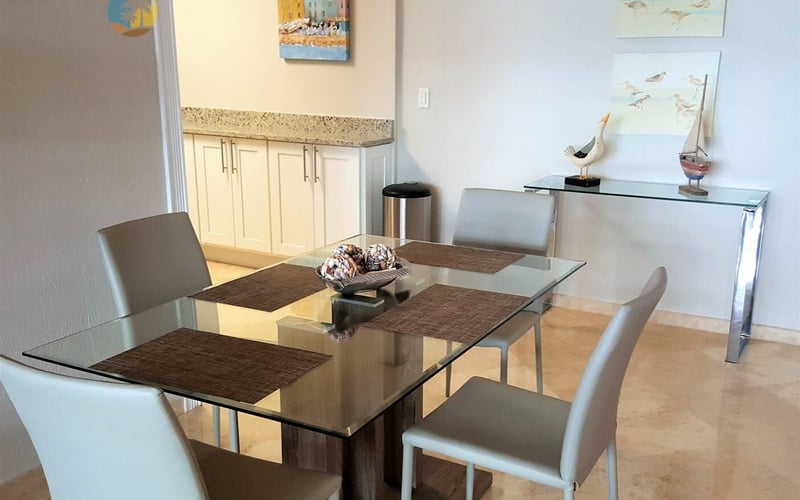 Modern dining room with glass table, gray chairs, cream cabinets, and nautical artwork on walls