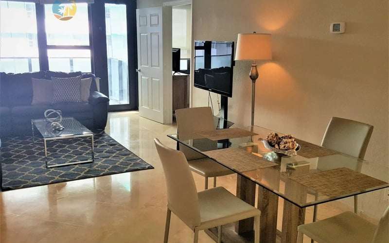 Open-plan condo with dining table, living room sofa, and ocean view through floor-to-ceiling windows