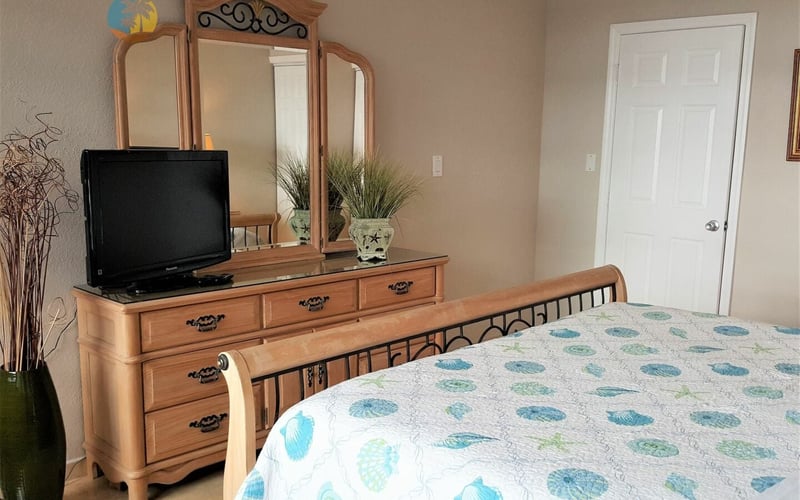 Bedroom with queen bed, wooden dresser with mirror and TV, white closet door, and coastal-themed decor