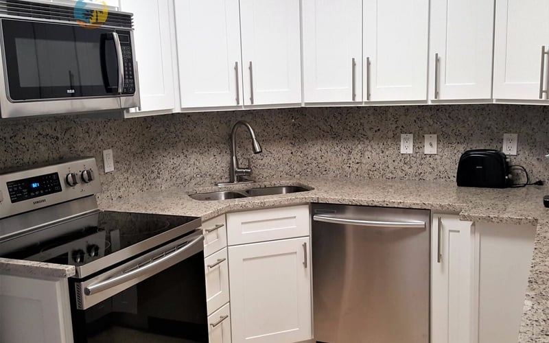 Modern kitchen with white cabinets, granite countertop, stainless steel appliances, and microwave mounted above stove.