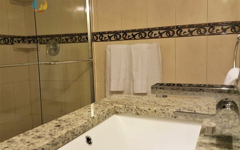 Bathroom with granite countertop, white sink, glass shower enclosure, and decorative tile border