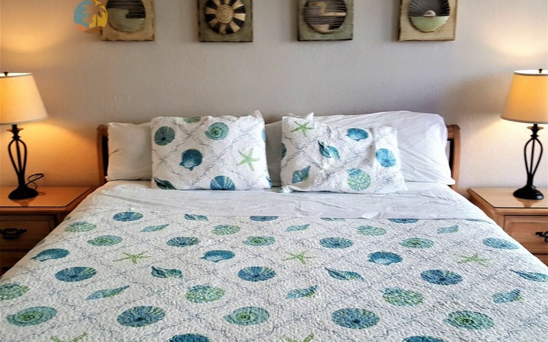 Bedroom with queen bed, shell-patterned bedding, wooden nightstands with yellow lamps, and four framed circular artworks on wall above headboard.